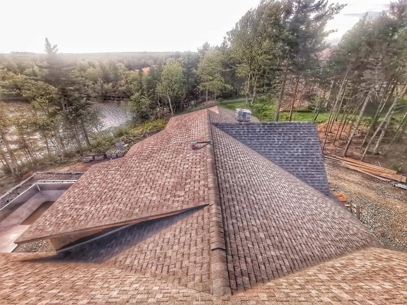 A finished shingle roof on a large home beside a lake, seen from above