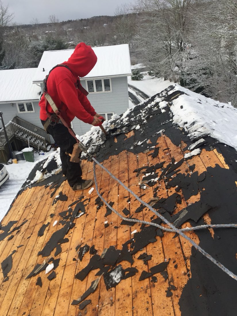 A Northline roofer stripping old shingles off a roof in the snow