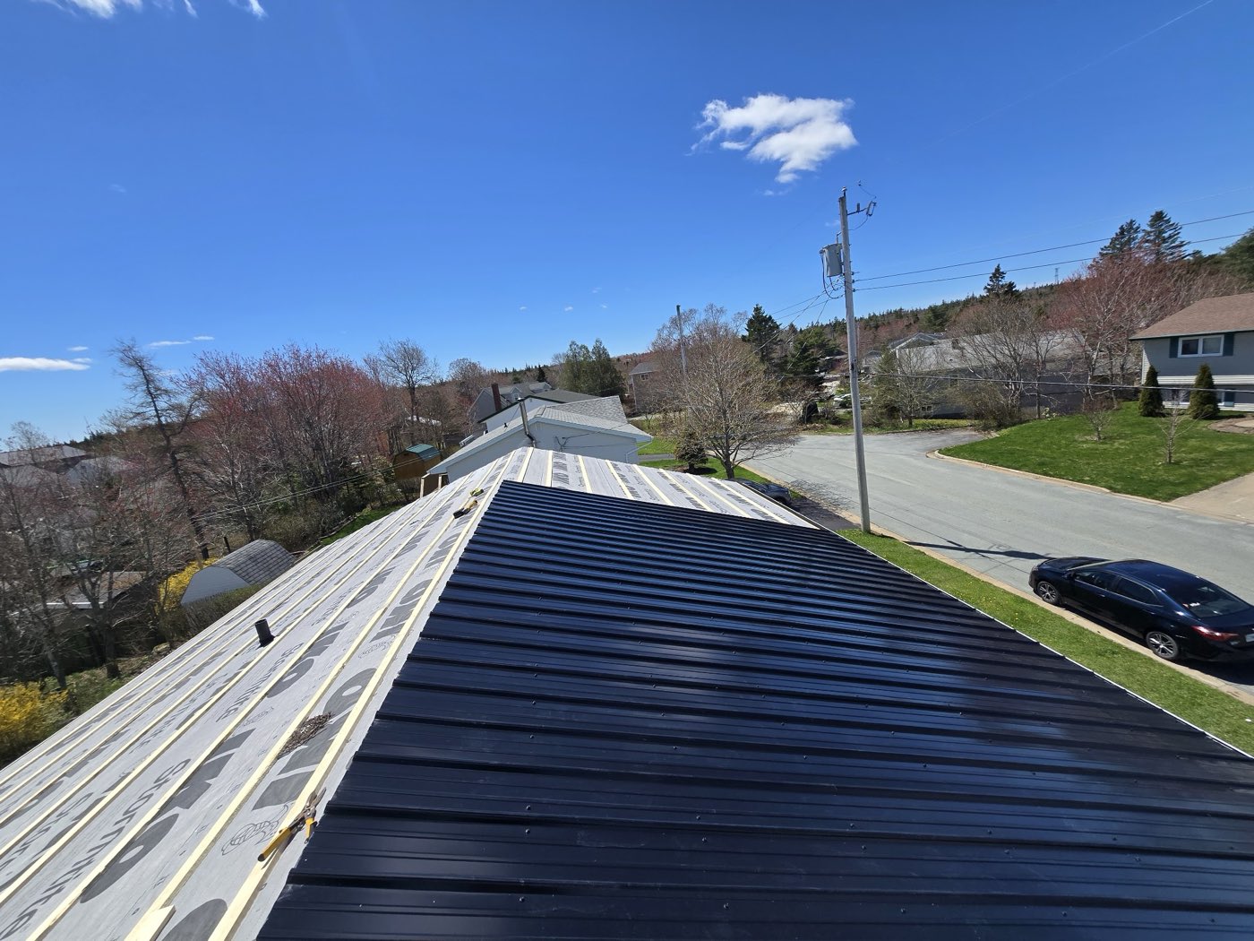 A steel roof going on over new strapping under a blue sky