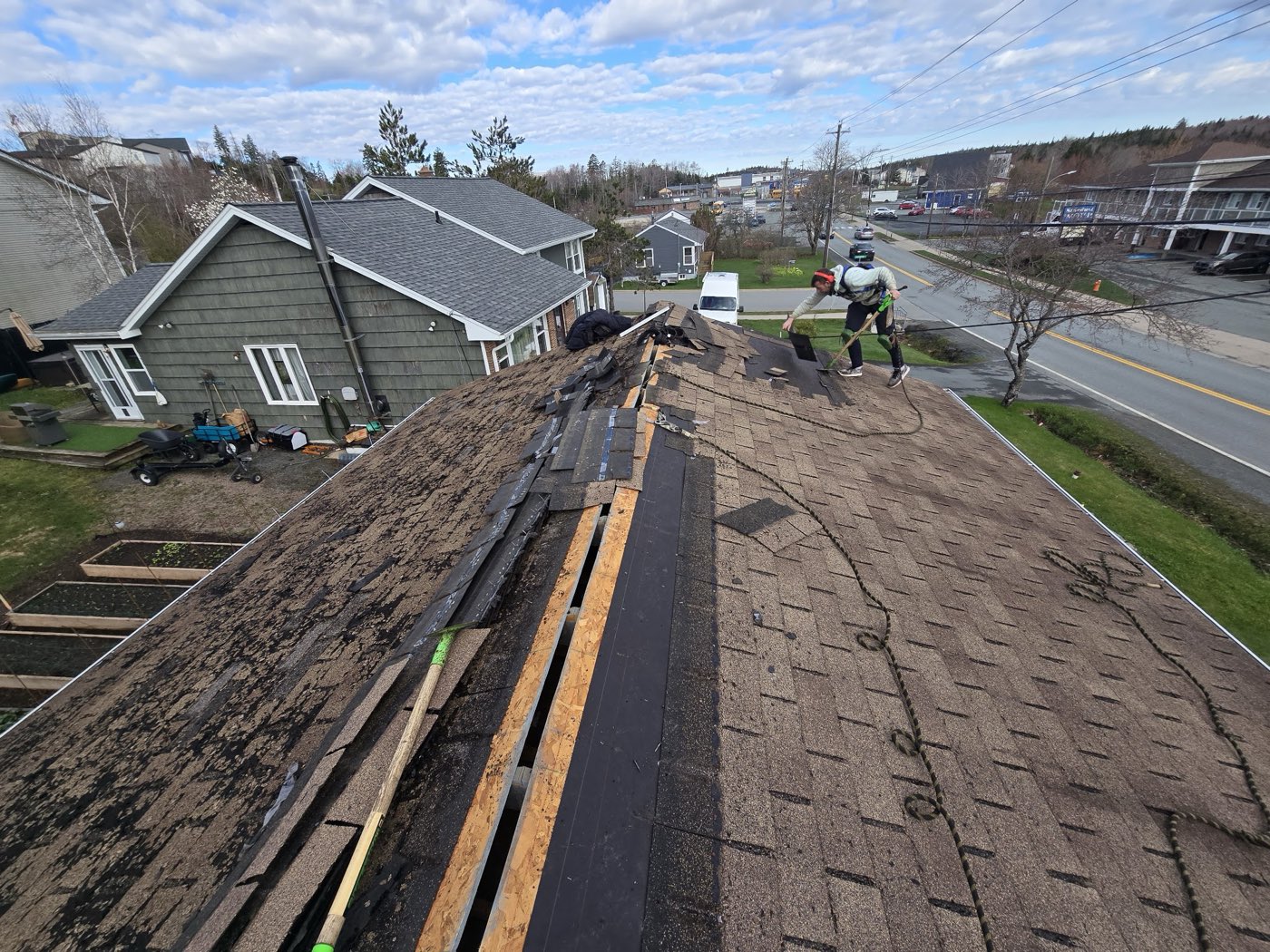 A roofer working on an older shingle roof mid tear-off