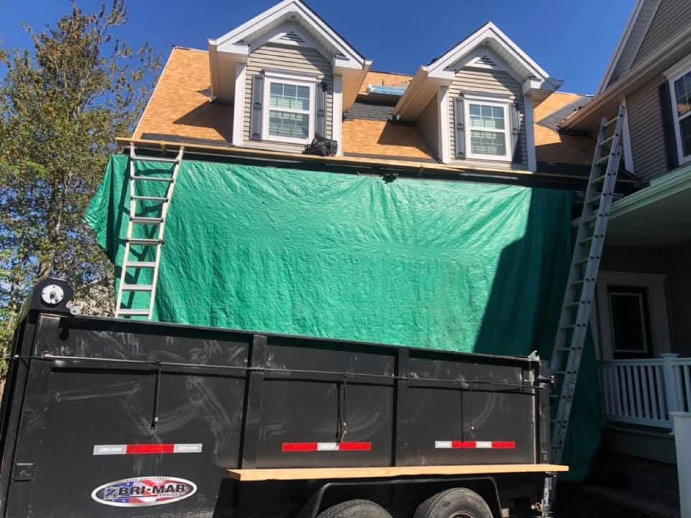 A roof job tarped off with a dump trailer parked in the driveway